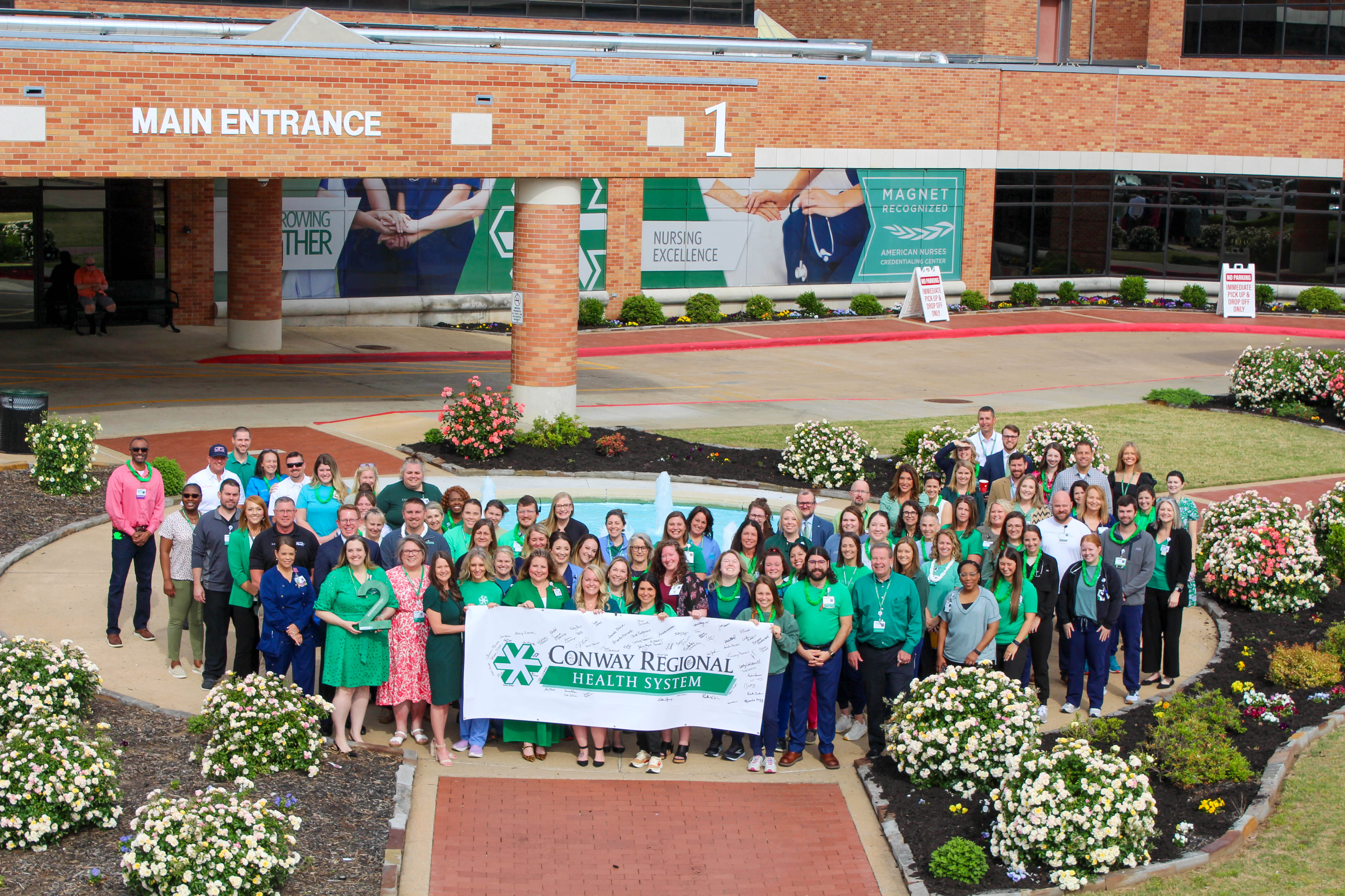 A group of employees stand outside the front of Conway Regional Hospital holding a Conway Regional banner that has signatures on it.